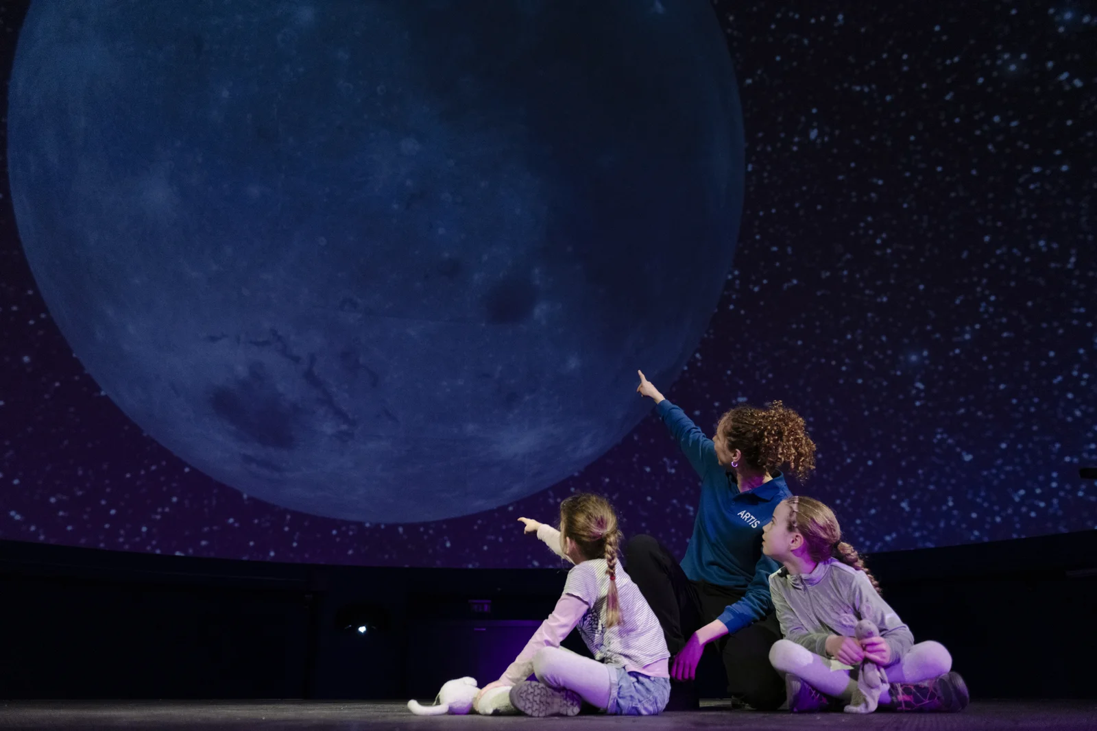 Visitors seated beneath the glowing full-dome projection of galaxies inside the Zeiss Planetarium at ARTIS Amsterdam